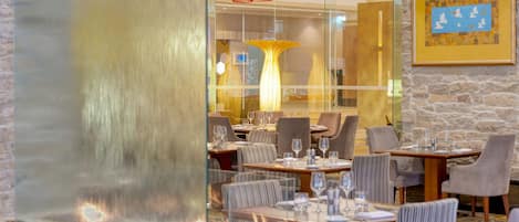 Un restaurante con mesas dispuestas para comer, un muro decorativo y un amplio ventanal.