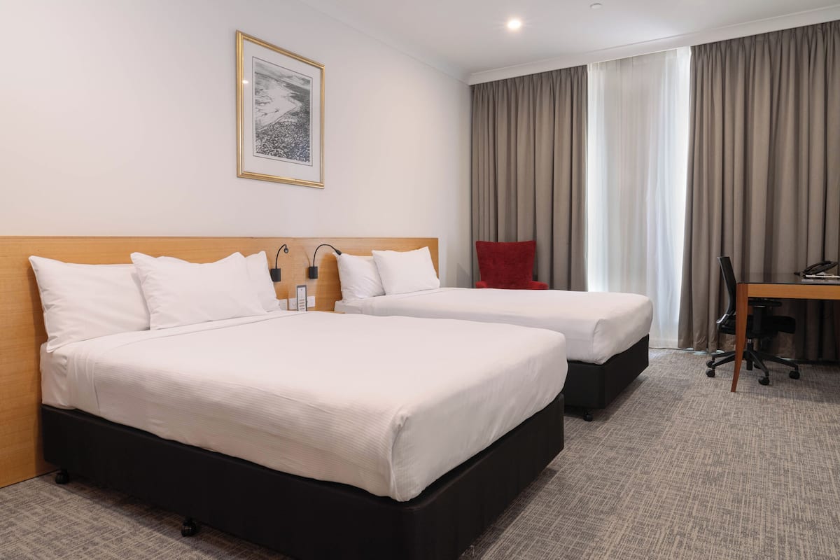 Habitació d'hotel amb dos llits, un escriptori, una cadira, una làmpada i un quadre al mur.