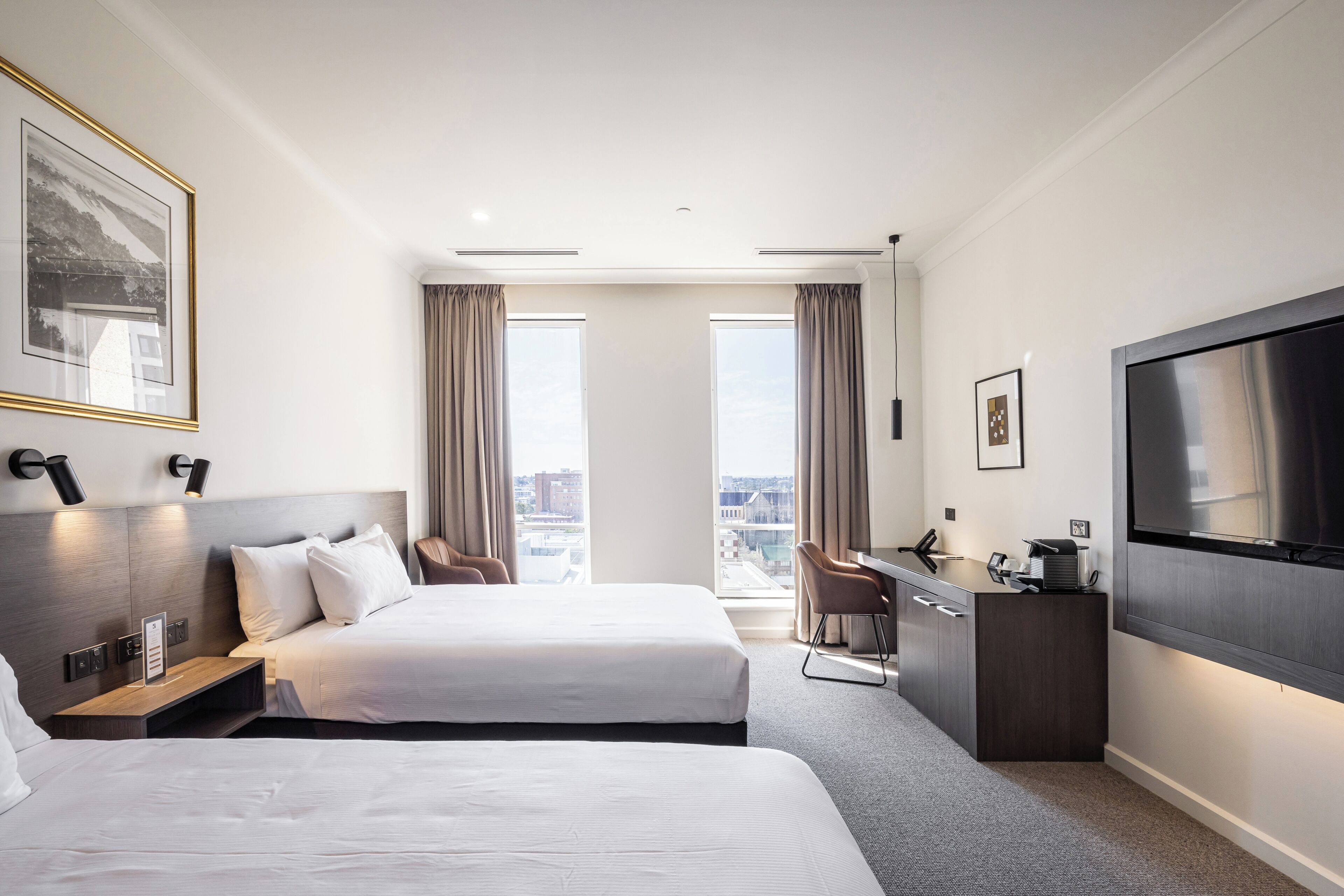 Habitación de hotel con dos camas, un escritorio, un televisor y vistas a la ciudad.