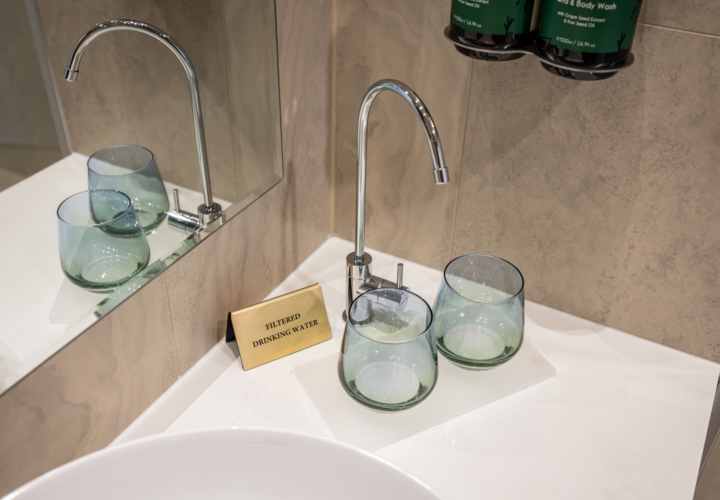Un lavabo de baño con un grifo moderno, dos vasos de vidrio y un cartel que indica agua filtrada para beber.