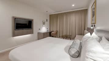 Ein modernes Hotelzimmer mit einem großen Bett, einem Schreibtisch, einem Stuhl, einem Fernseher und einem großen Fenster mit Vorhängen.