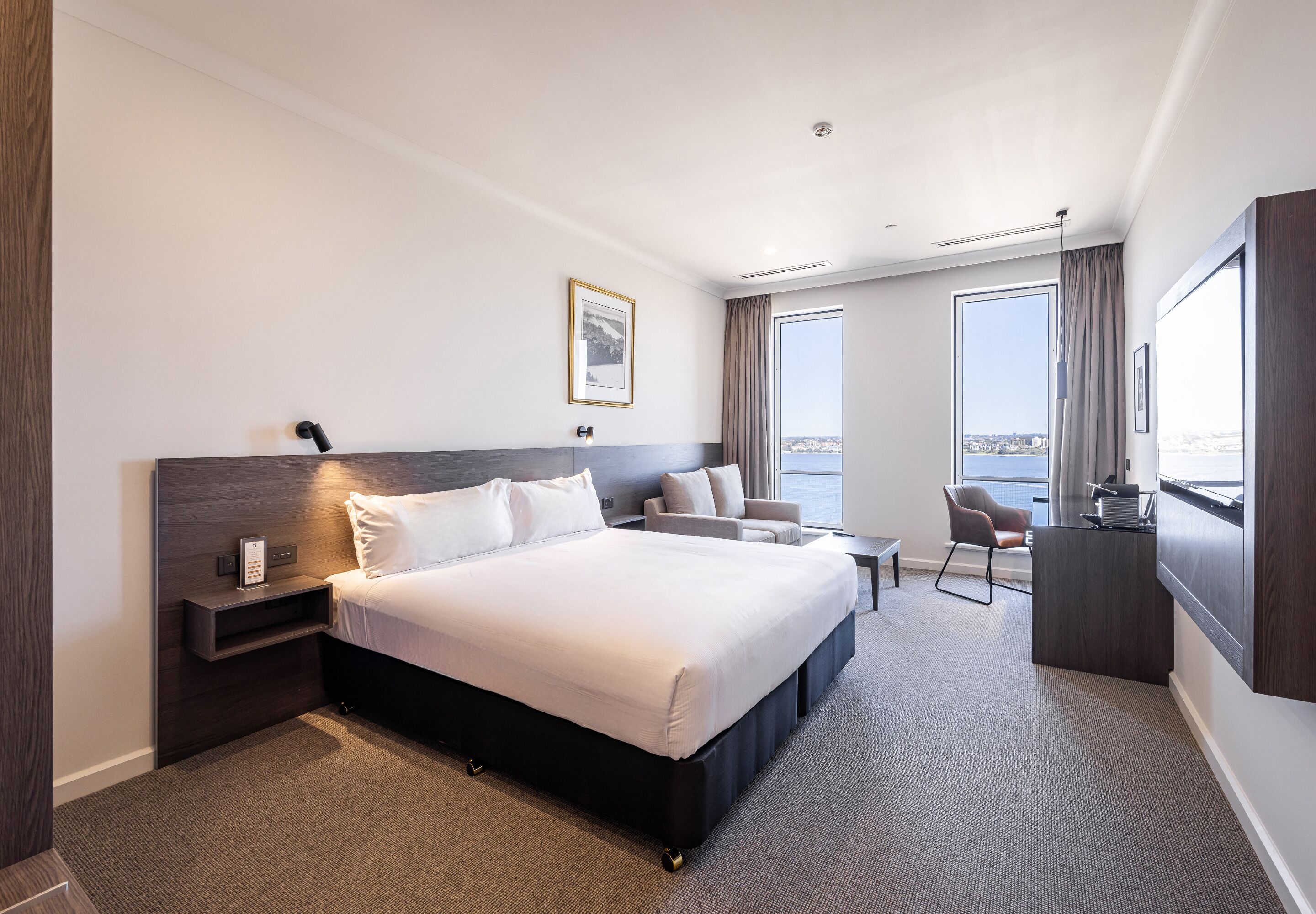 A modern hotel room with a large bed, a desk, a chair, and a view of the city.