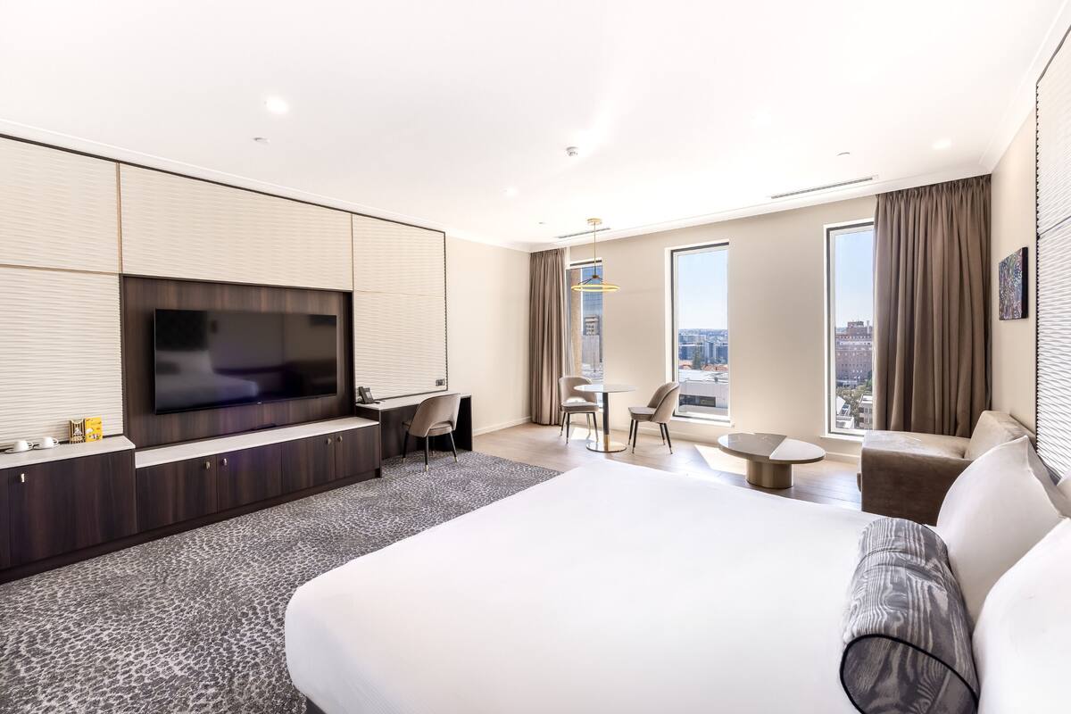 Habitació d'hotel moderna amb un llit gran, televisió de pantalla plana, escriptori i zona de seients amb vista a la ciutat.