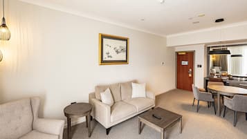 Una habitación de hotel moderna con un sofá color beige, una mesa redonda y un rincón de comedor con una mesa y sillas.