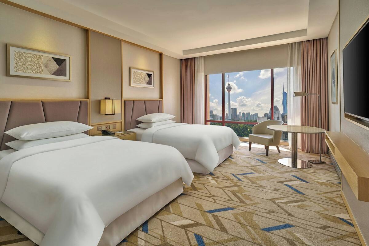 A hotel room with two beds, a small table, a chair, and a city view.