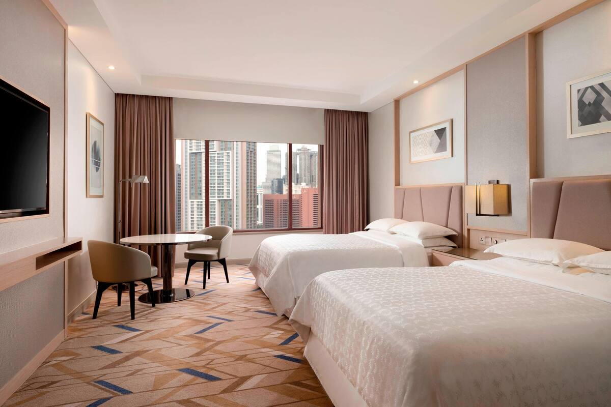 A hotel room with two beds, a TV, a desk, and a chair.
