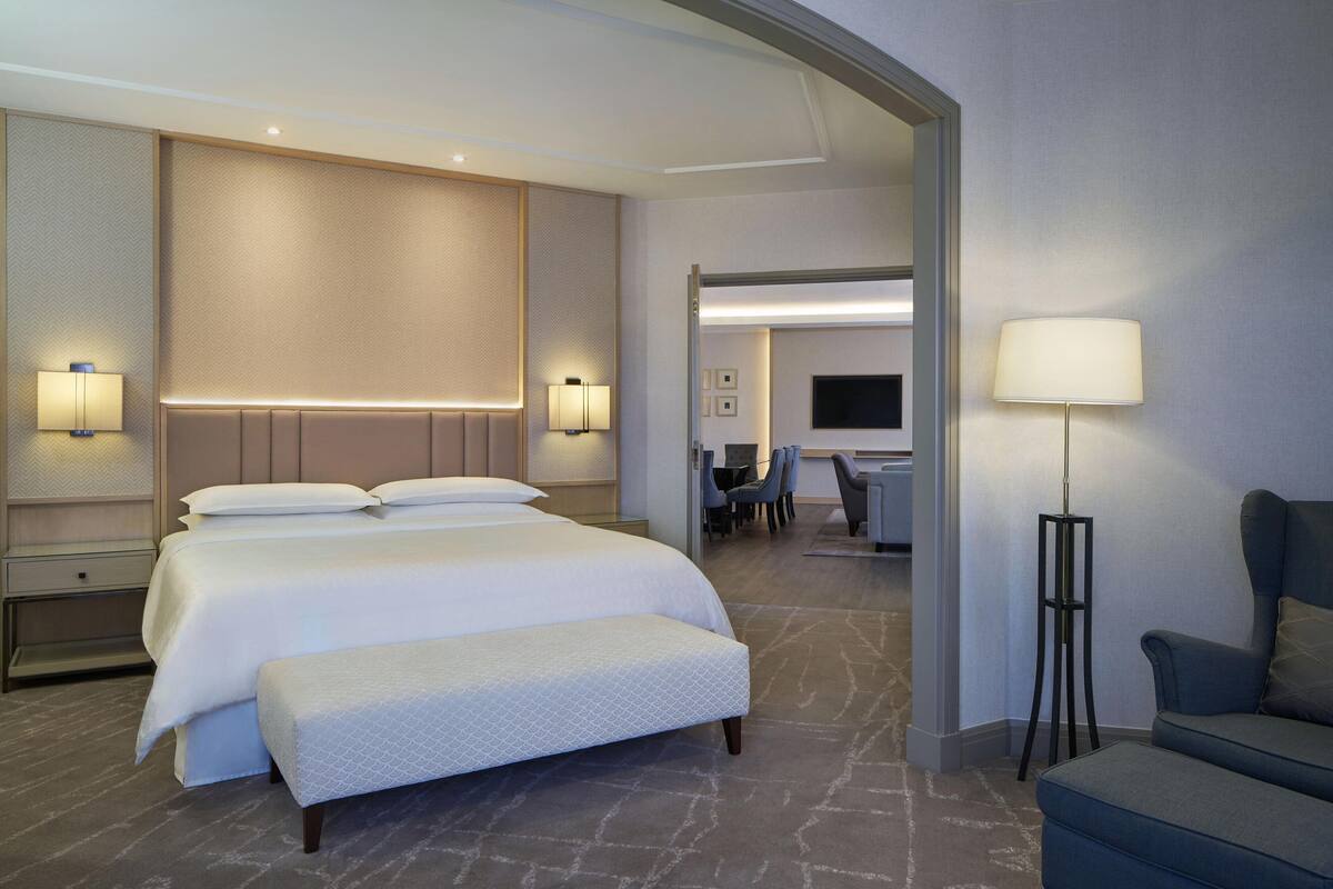 A modern hotel room with a large bed, bedside lamps, a desk with chairs, and a TV.