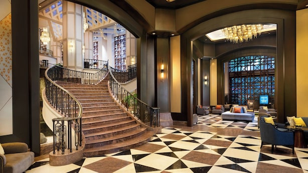 A grand lobby with a marble staircase, a checkered floor, and a seating area with sofas and a television.