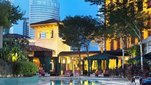 A pool area with lounge chairs, a building with a tiled roof, and a reflection in the water.