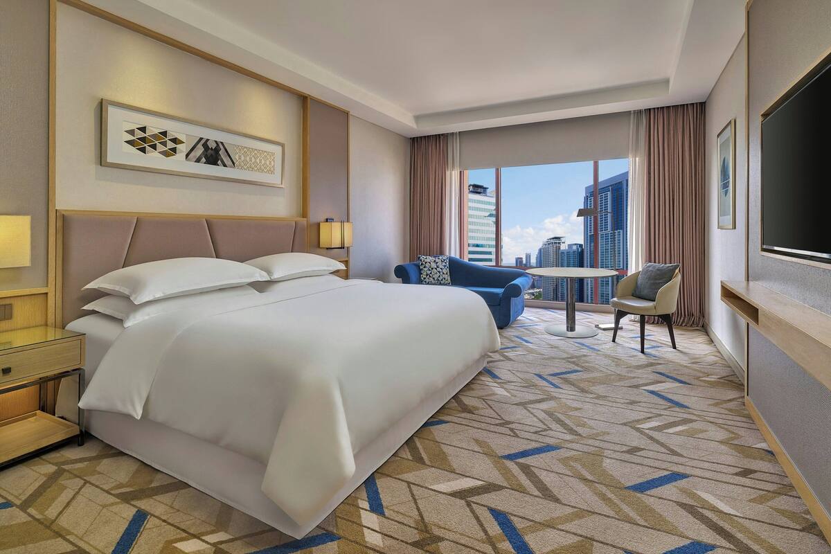 A hotel room with a large bed, a sofa, a small table, and a TV.
