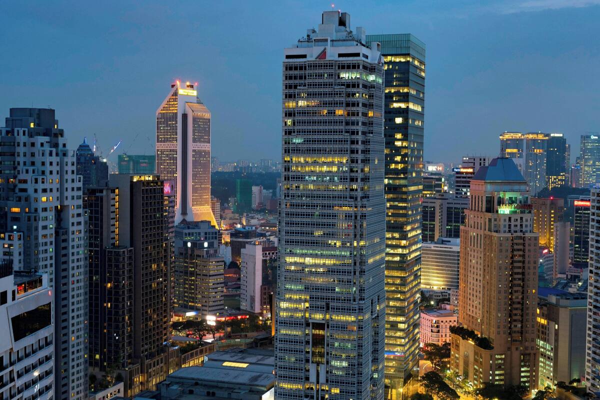 A cityscape with high-rise buildings, including a prominent skyscraper with illuminated windows and a distinctive spire.