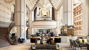 A spacious lobby with a grand staircase, a chandelier, and a seating area with sofas and tables.