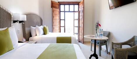 A hotel room with two beds, a television, a table with a chair, and a balcony with open doors.