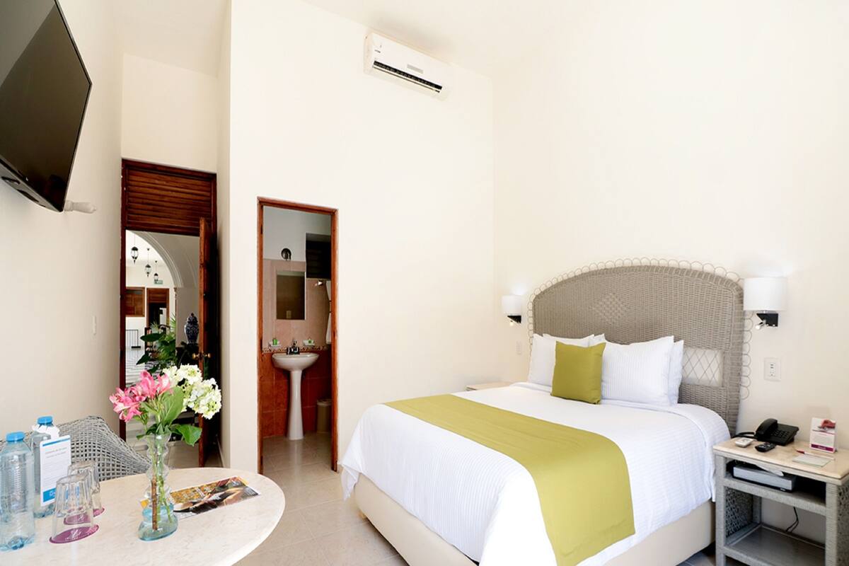 Una camera d'albergo con un letto, comodino, televisione e bagno visibile tramite una porta aperta.