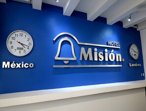 A hotel sign with the name "Misión" and "HOTEL" on a blue wall, along with clocks and the words "México" and "Londres".
