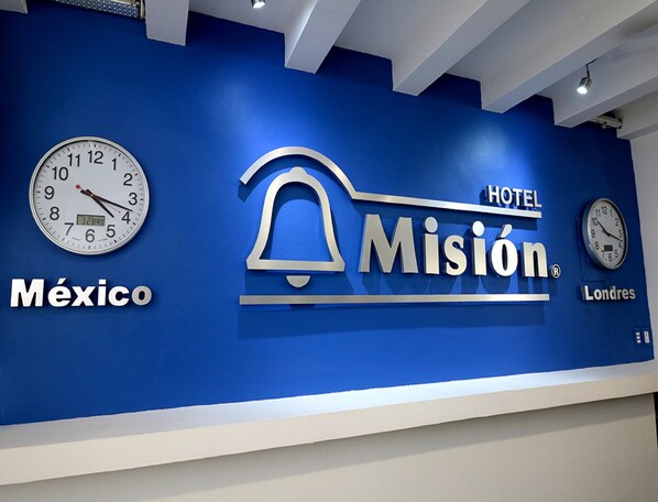 A hotel sign with the name "Misión" and "HOTEL" on a blue wall, along with clocks and the words "México" and "Londres".