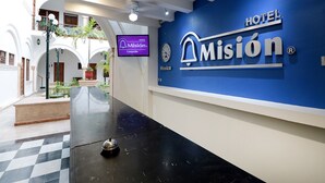 Zona de recepción de un hotel con mostrador de registro, un reloj y un cartel que dice 'HOTEL Misión'.