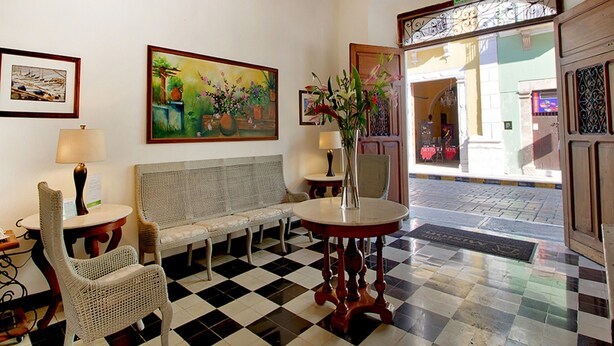 Un vestíbulo con piso a cuadros, un candelabro, muebles de mimbre y un cuadro.
