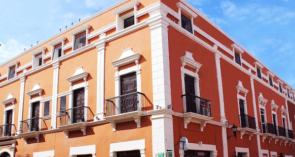 A multi-story building with white and orange exterior walls, multiple balconies with black railings, and a clear blue sky in the background.