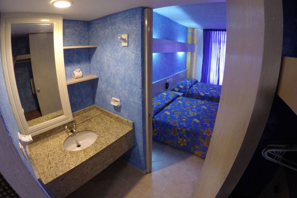 Una habitación de hotel con baño, una cama y una mesita de noche.
