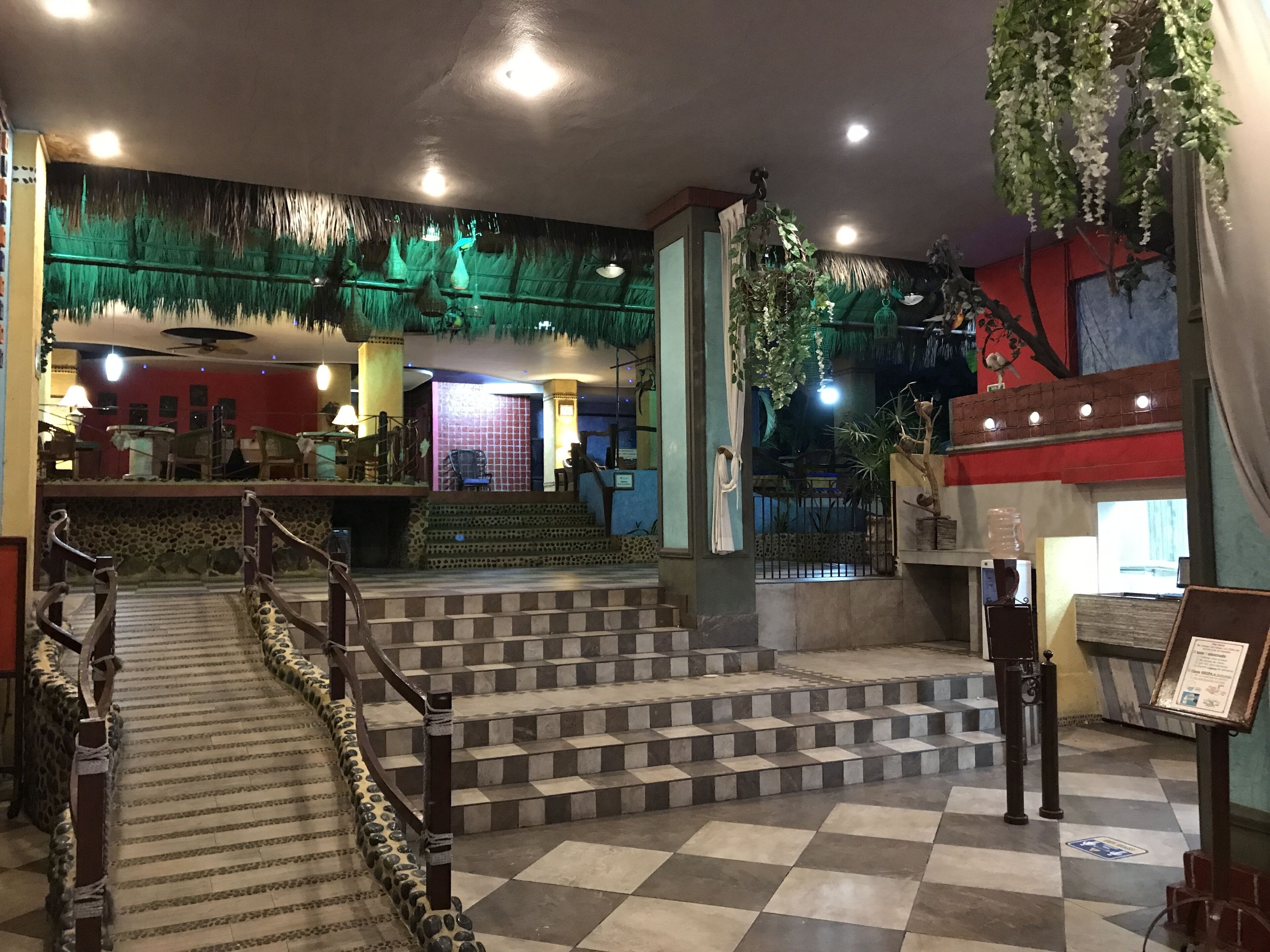 A hotel lobby with a checkered floor, a staircase leading to a second floor, and a reception desk.