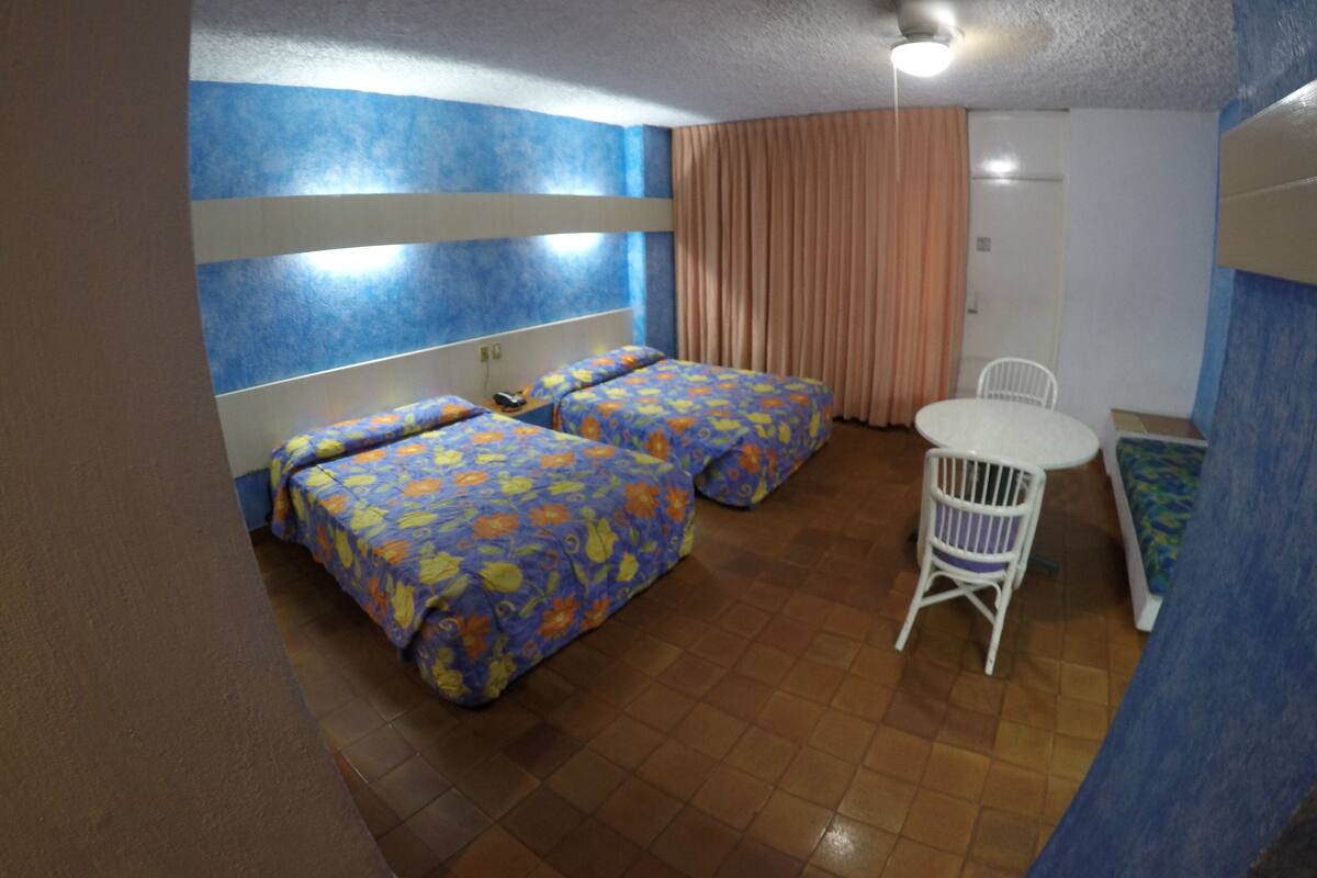 Una habitación con dos camas, una mesita y una silla.