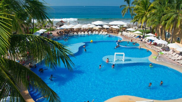 A large outdoor swimming pool with multiple lanes, surrounded by lounge chairs and umbrellas, and overlooking the ocean.