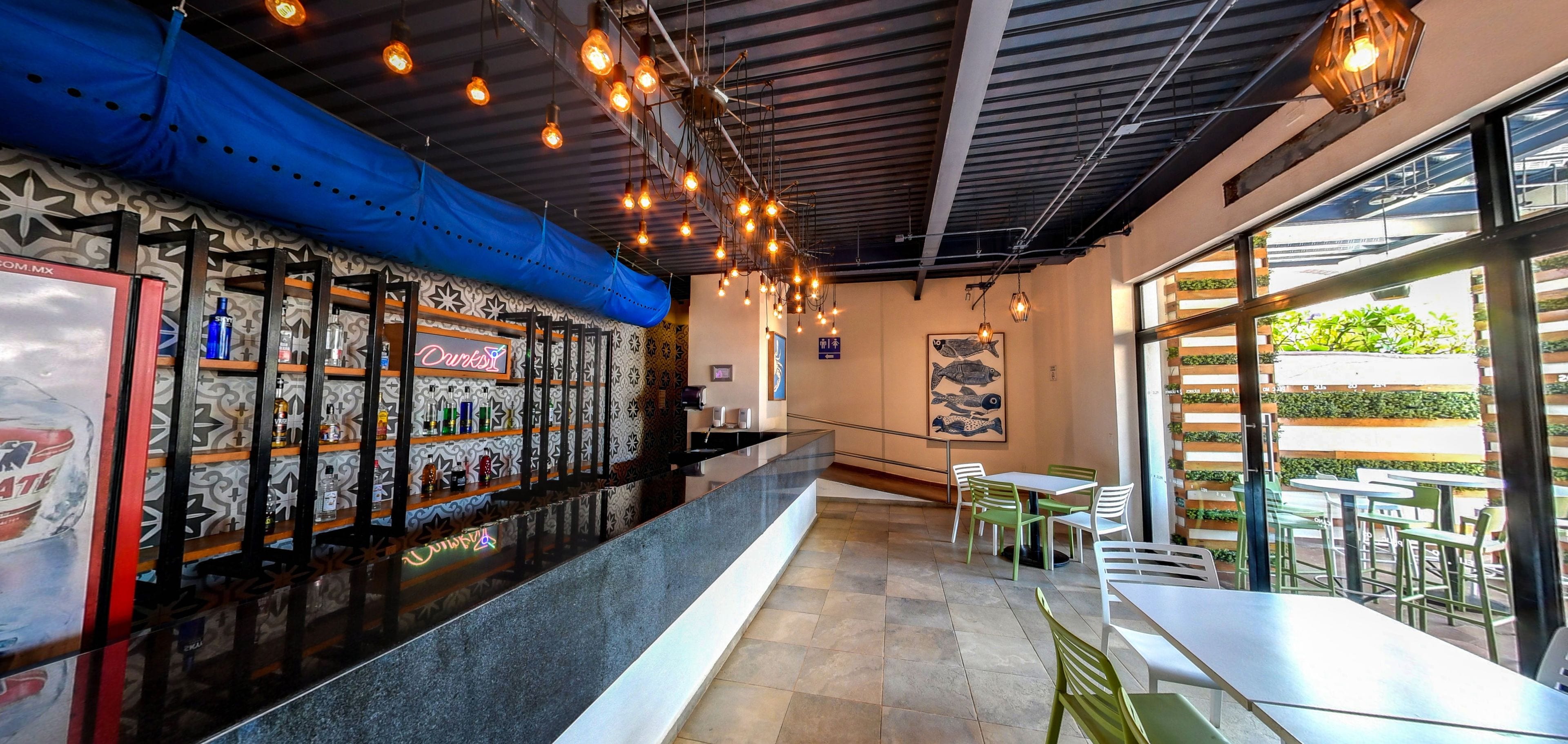 Interior de un restaurante con barra, asientos y vistas amplias a través de grandes ventanales.