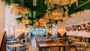 A spacious restaurant with high ceilings, hanging wicker chandeliers, and a variety of seating options including tables and chairs.