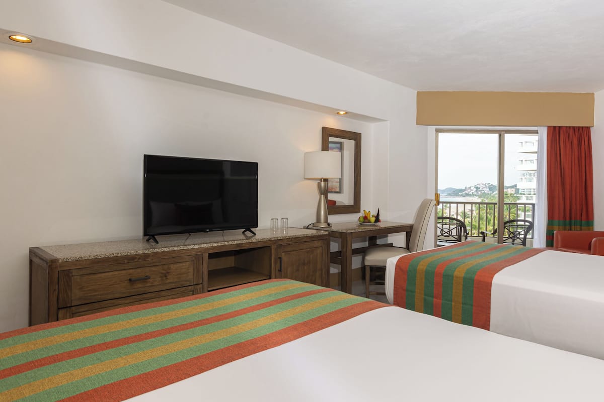 A hotel room with two beds, a TV, a desk, and a balcony with a view.