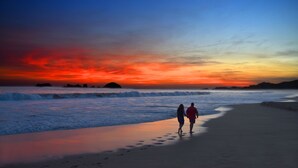 A beach scene with two people walking along the shore during sunset. - Tesoro Ixtapa All Inclusive (Ixtapa)