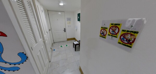 A hallway with a white door at the end, a small table with papers, and a wall with multiple 'NO GRITO' signs.