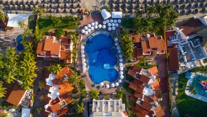 An aerial view of a resort with multiple swimming pools, palm trees, and beach umbrellas.