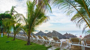 A beachside lounge area with white lounge chairs and thatched umbrellas, overlooking the ocean.