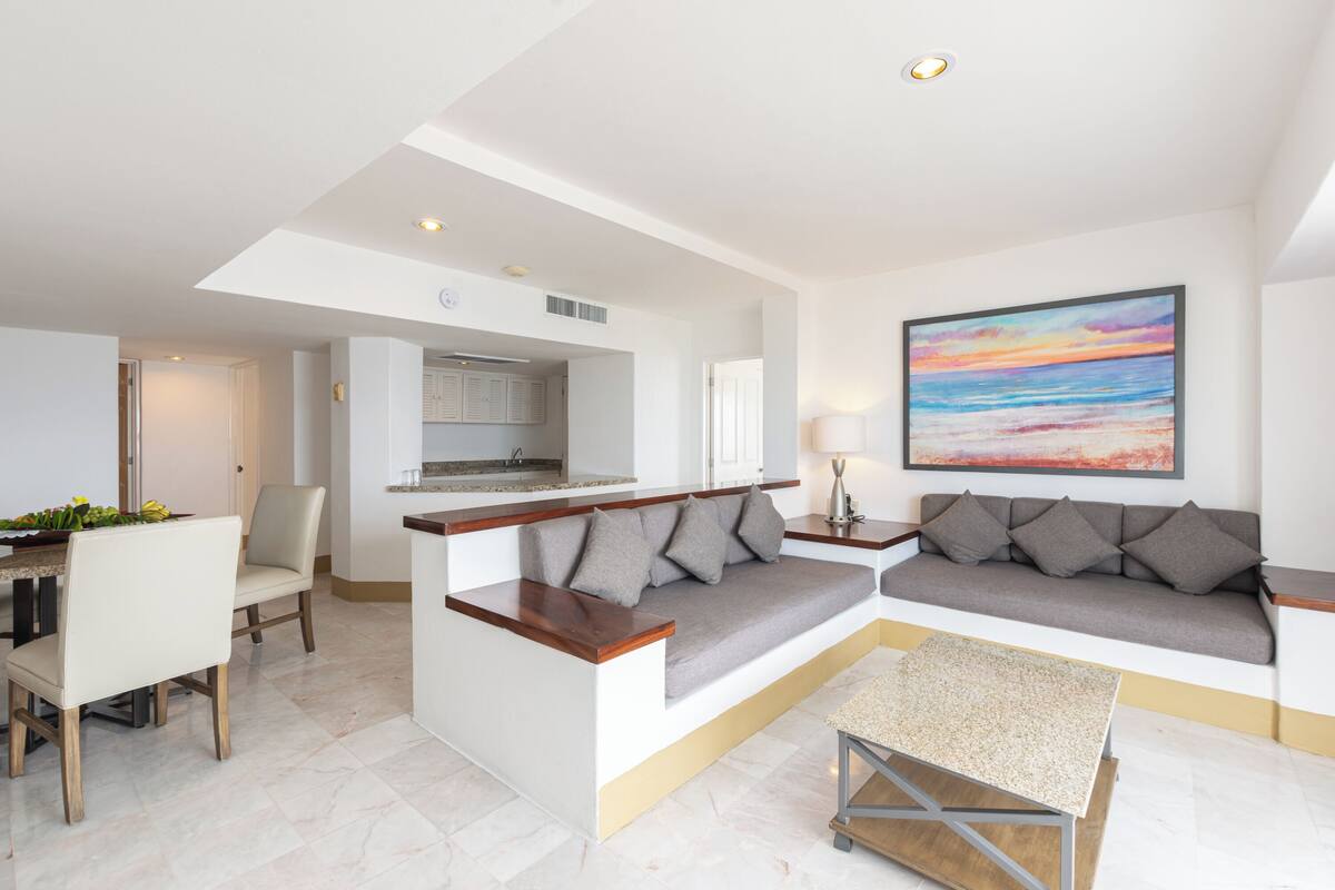 A modern living room with a sofa, a dining table, and a kitchen in the background.