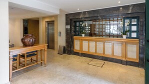 En entréhall med ett marmorgolv, en receptionsdisk i trä, en krukväxt och en glasdörr med utsikt.