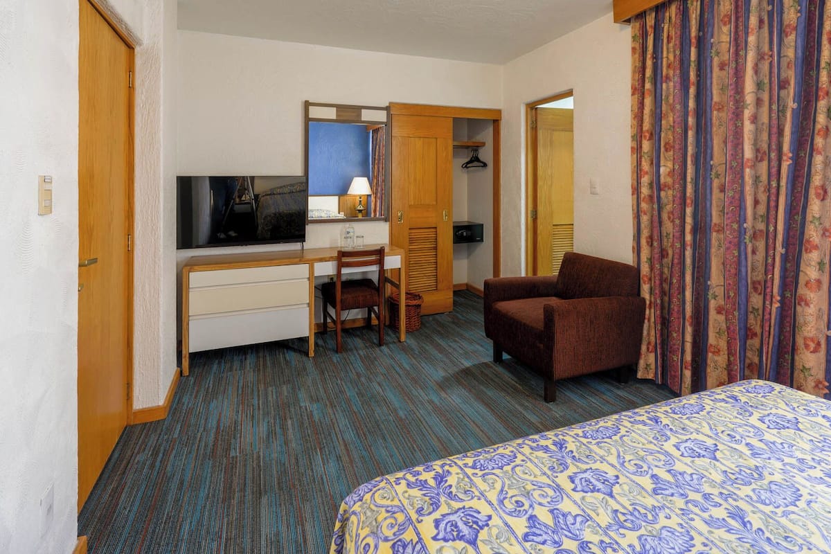A hotel room with a bed, a desk with a computer, a chair, and a television.