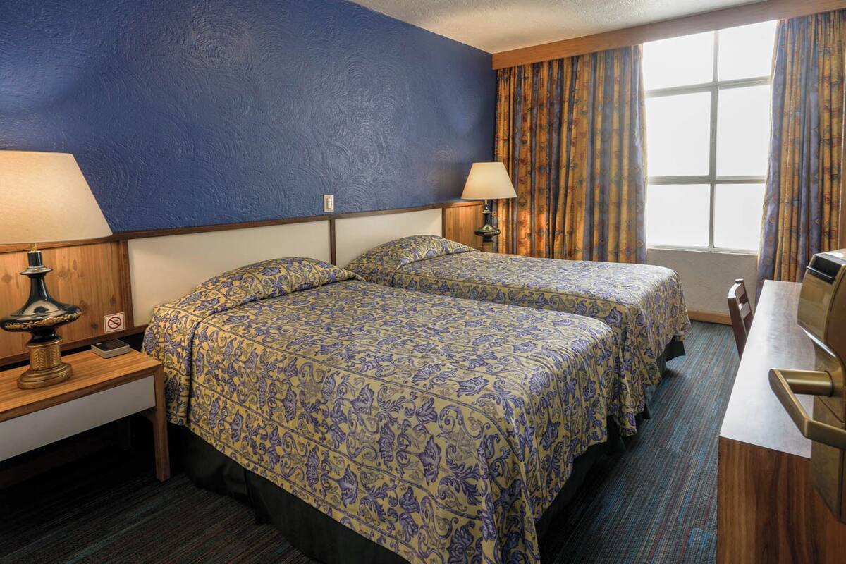 A hotel room with two beds, a desk, a lamp, and a window with curtains.