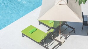 A poolside area with a lounge chair, an umbrella, and a chair. - Ports of Call Resort Turks, Tapestry Collection by Hilton (Providenciales)