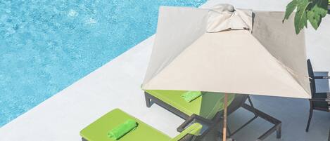 Zona junto a la piscina con una tumbona, una sombrilla y una silla.