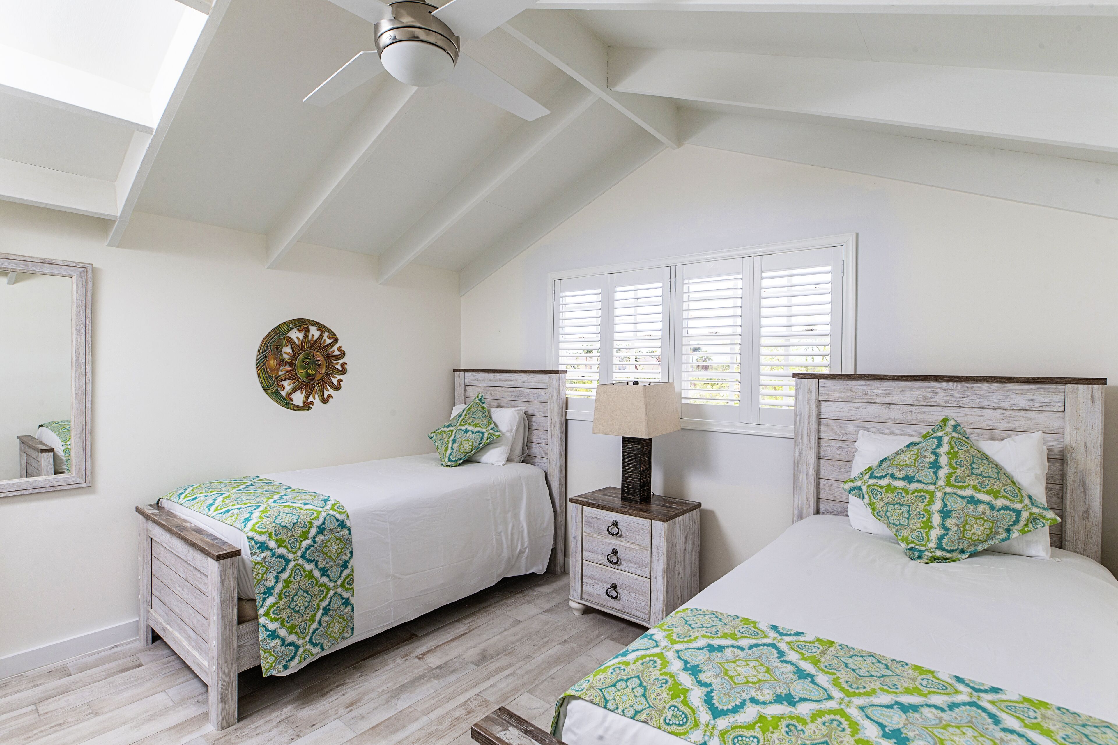 A bedroom with two beds, a ceiling fan, a nightstand, and a window with blinds.