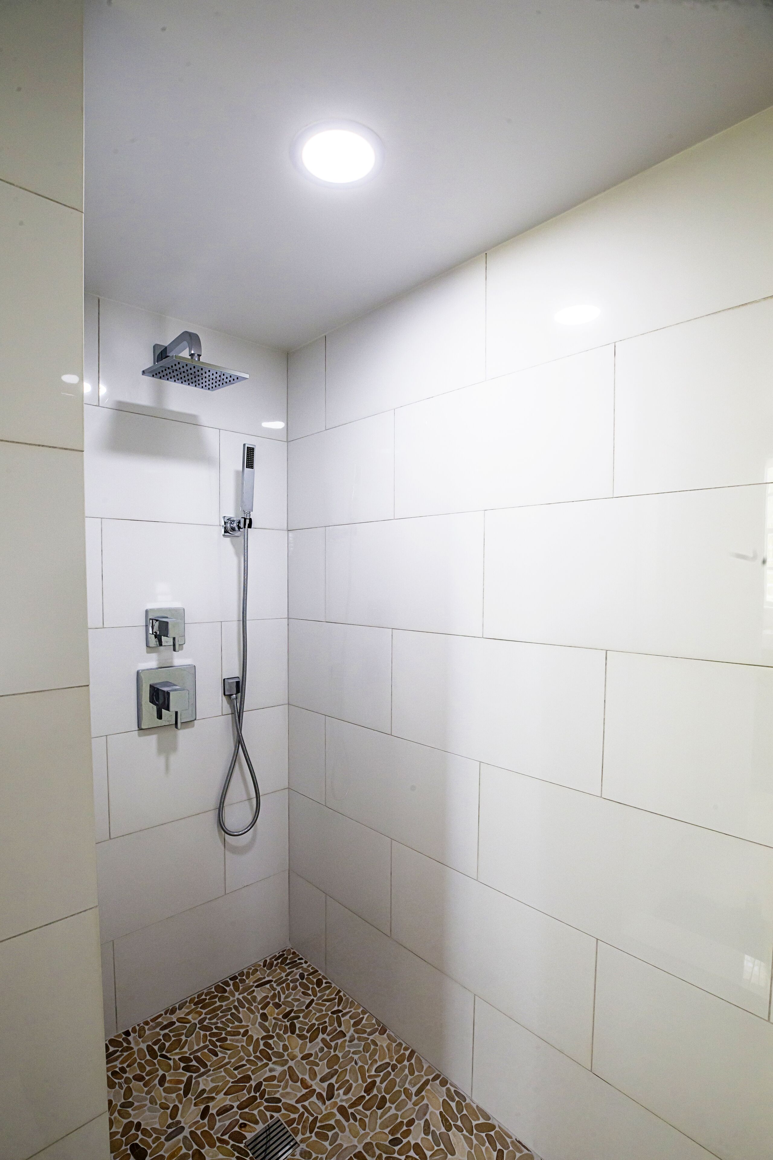 A shower with a handheld showerhead and a wall-mounted faucet, tiled walls, and a patterned floor.
