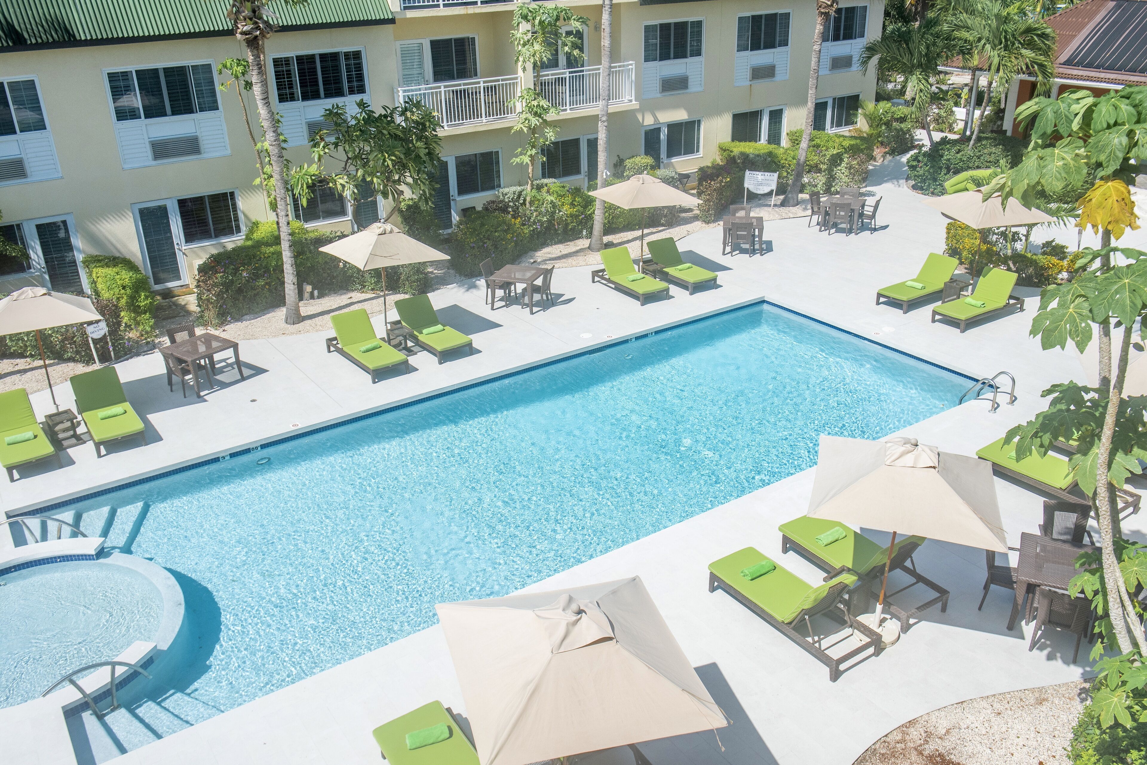 Ein Swimmingpool mit Liegestühlen und Sonnenschirmen, umgeben von einem Gebäude mit Balkonen und Palmen.