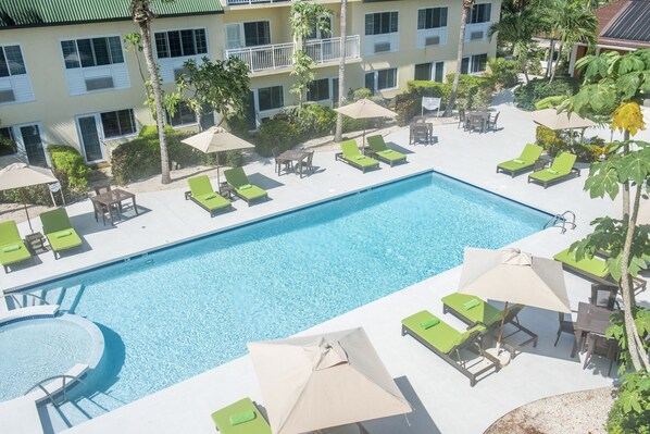 A swimming pool with lounge chairs and umbrellas, surrounded by a building with balconies and palm trees. - Ports of Call Resort Turks, Tapestry Collection by Hilton (Providenciales)