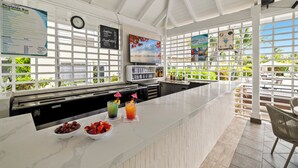 A clean, modern bar area with a white marble countertop, a clock, and a menu board. - Ports of Call Resort Turks, Tapestry Collection by Hilton (Providenciales)