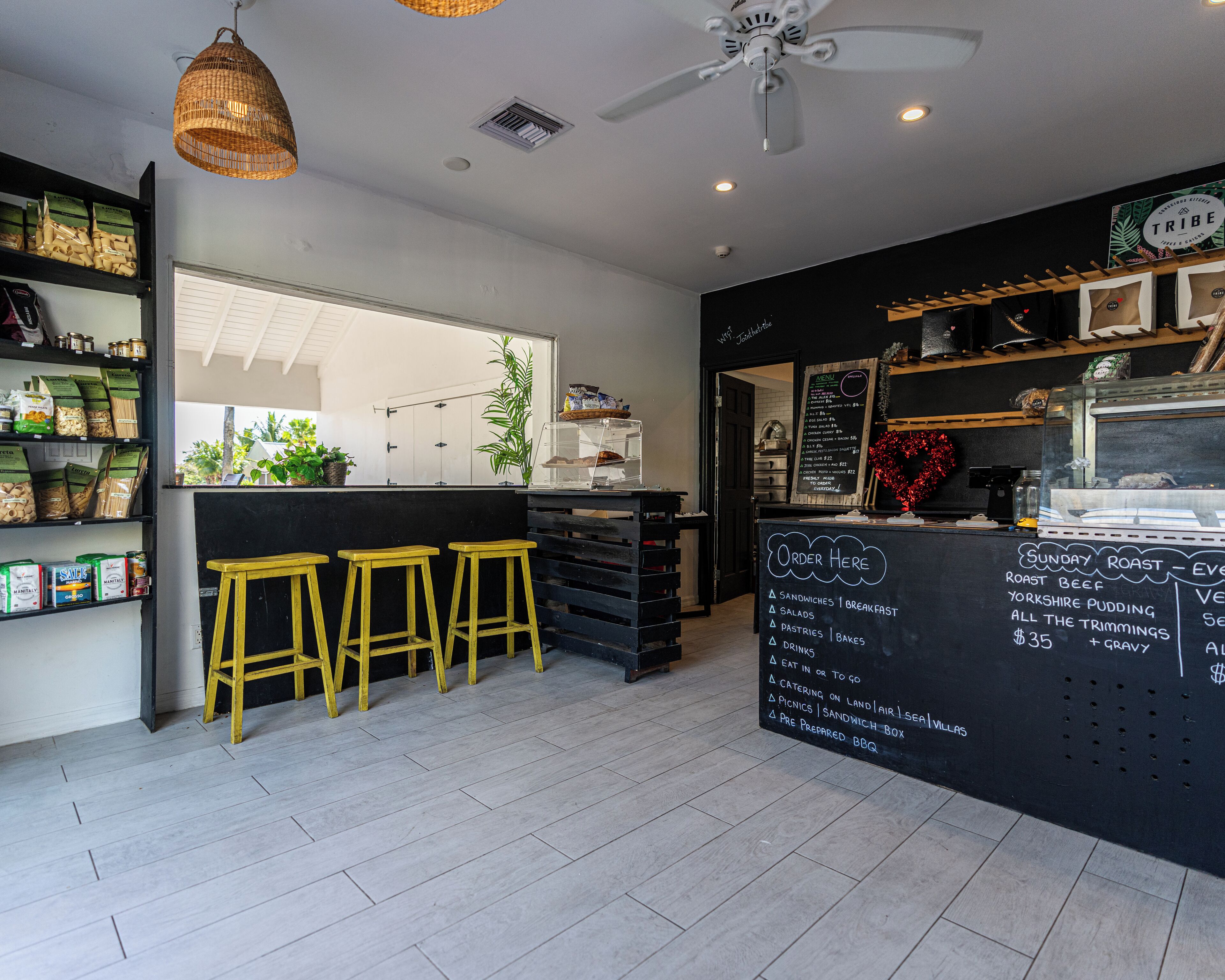 Un café avec un comptoir noir, des tabourets jaunes et un tableau affichant le menu.