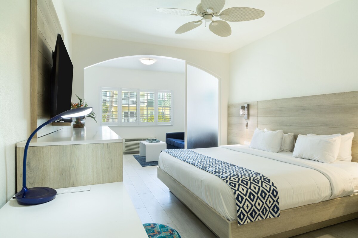 Een moderne hotelkamer met een groot bed, een bureau met lamp, een plafondventilator en uitzicht.