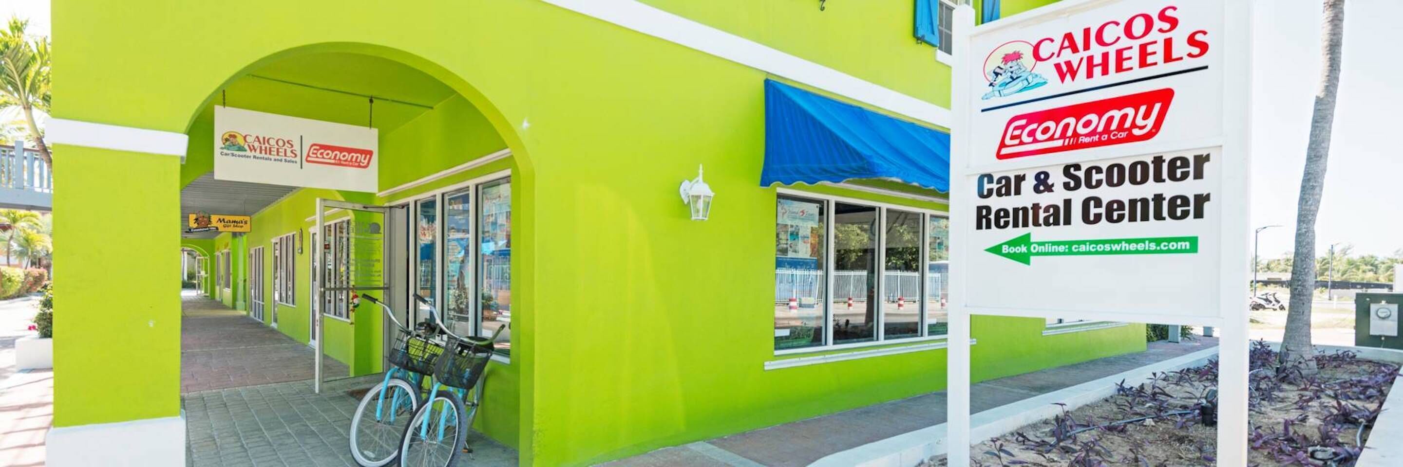 A bright green building with a sign for Caicos Wheels Car & Scooter Rental Center.