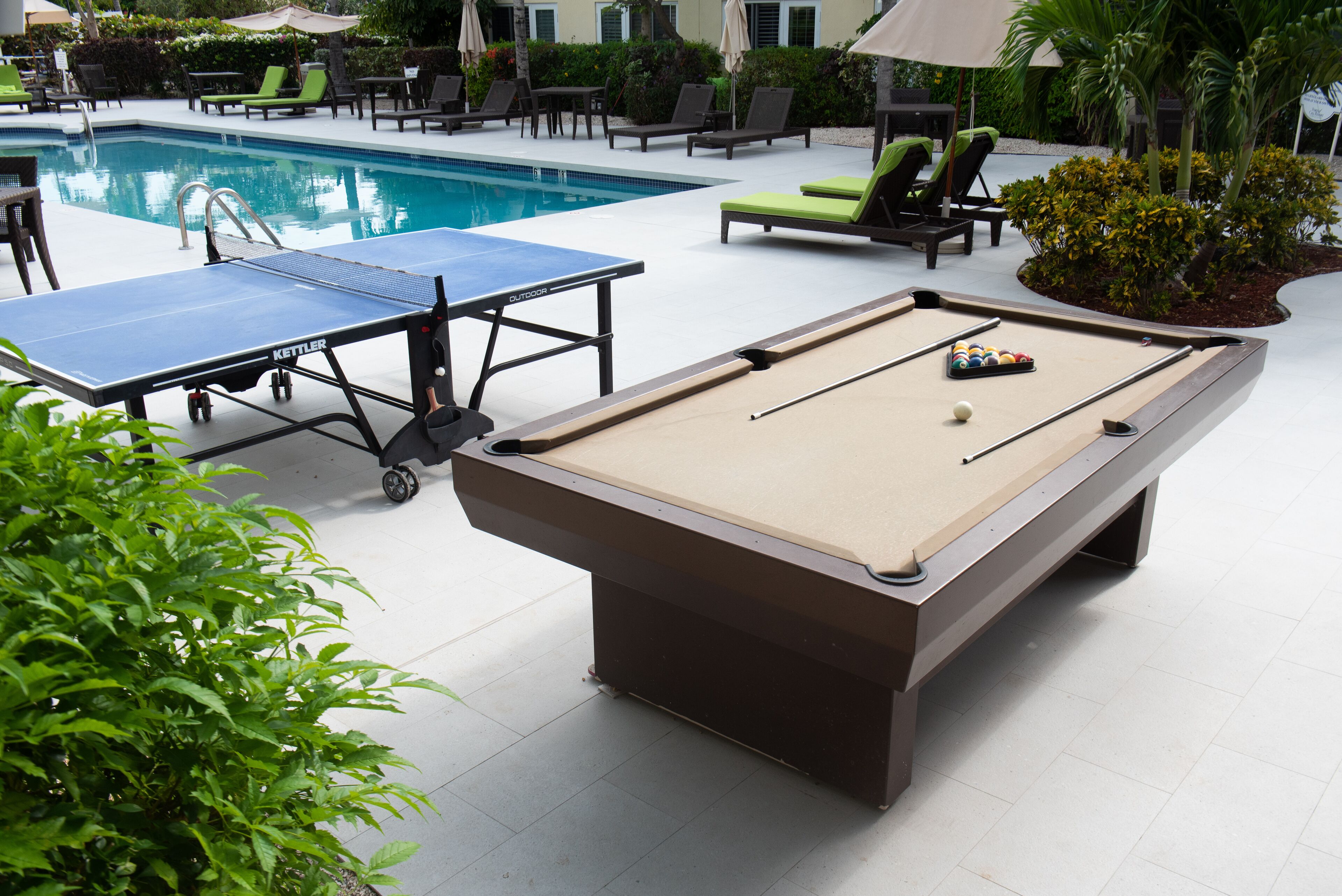 An outdoor pool area with a pool table, lounge chairs, and a small table tennis table.