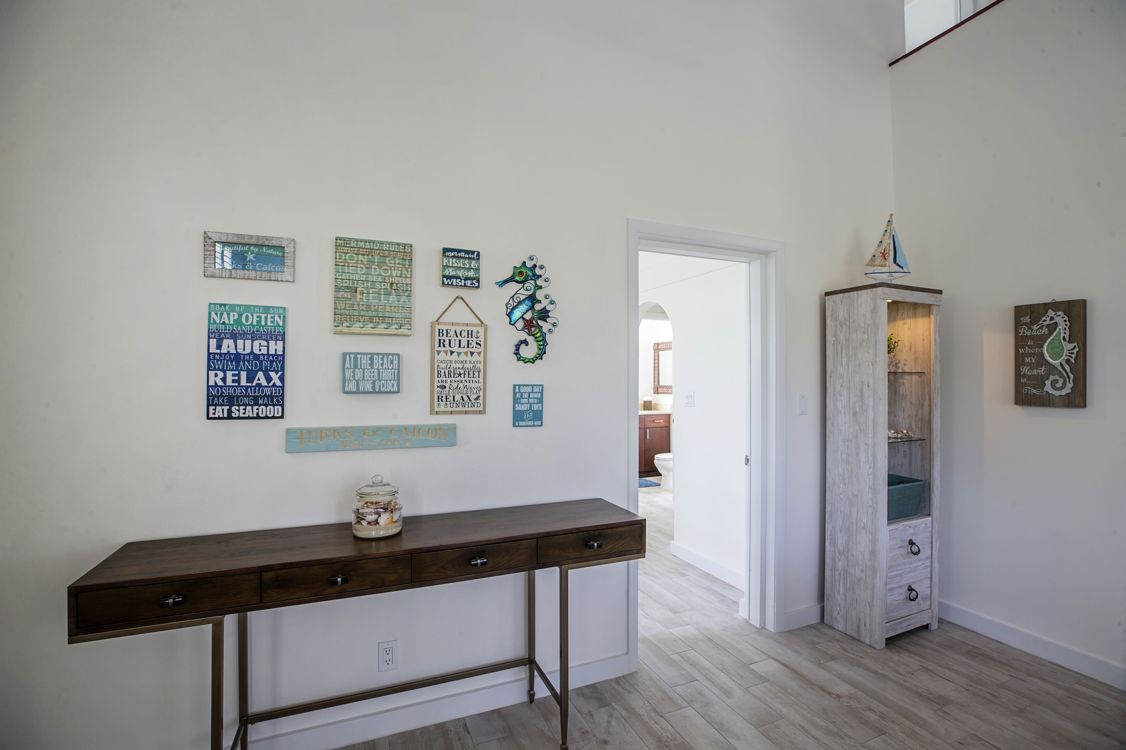 A hallway with a wooden console table, a cabinet, and various wall decorations including signs with phrases like "NAP OFTEN" and "RELAX."